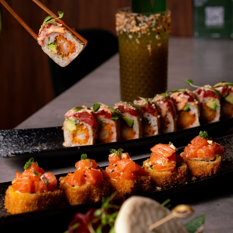 Chopsticks holding a sushi roll above a platter of Sushi Jungle rolls and salmon nigiri.
