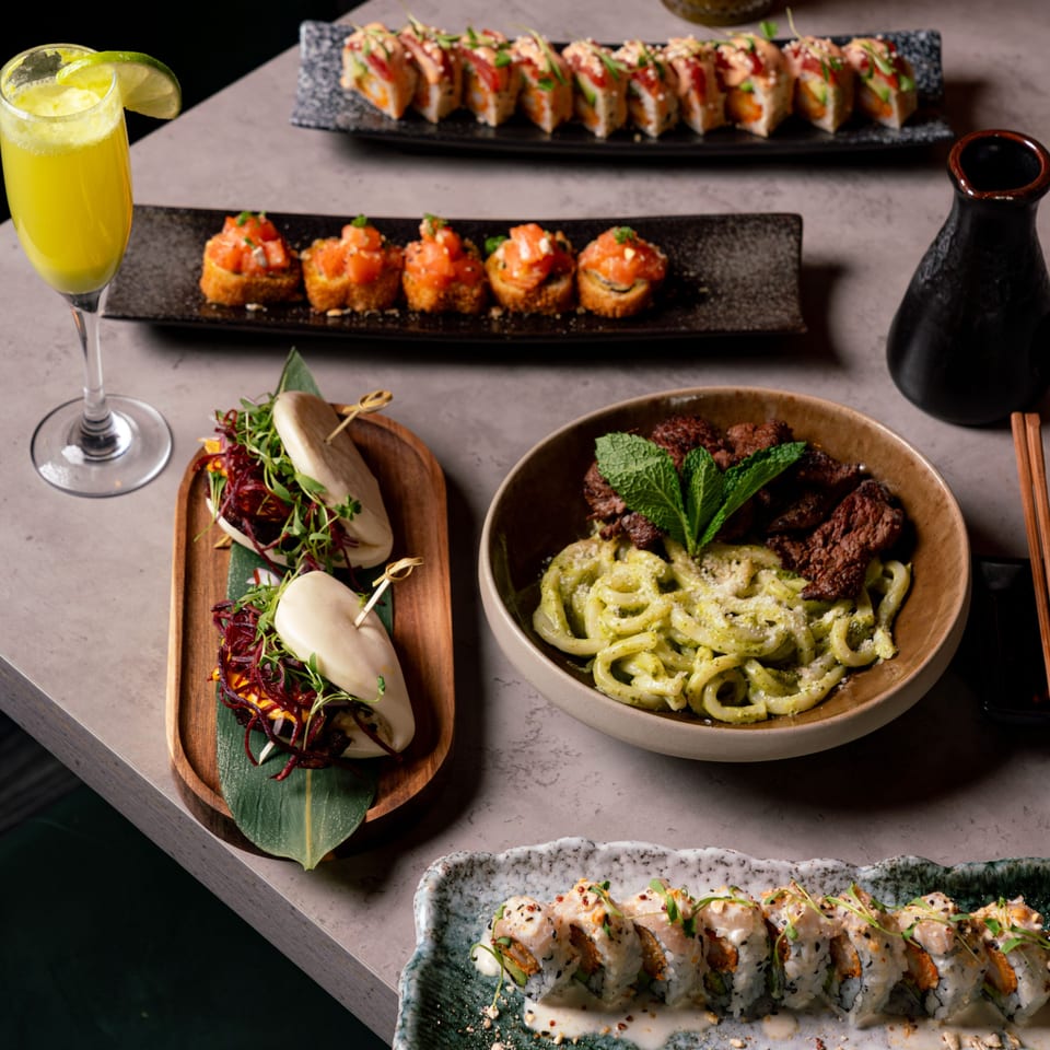 A table laden with various Sushi Jungle dishes, including sushi rolls, bao buns, and a noodle dish.